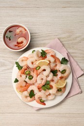 Photo of Tasty boiled shrimps with cocktail sauce, chili, parsley and lemon on light wooden table, flat lay