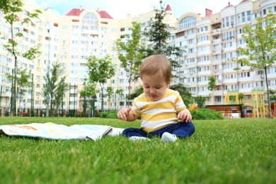 Photo of Adorable little baby sitting on green grass outdoors