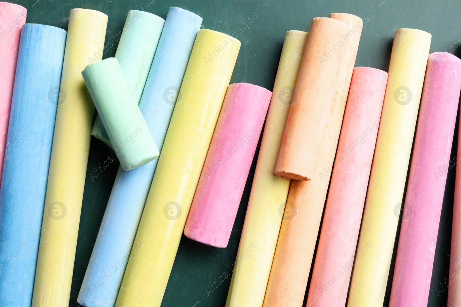 Photo of Pieces of color chalk on greenboard, flat lay