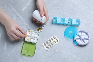 Woman putting pill into plastic box at grey marble table, top view