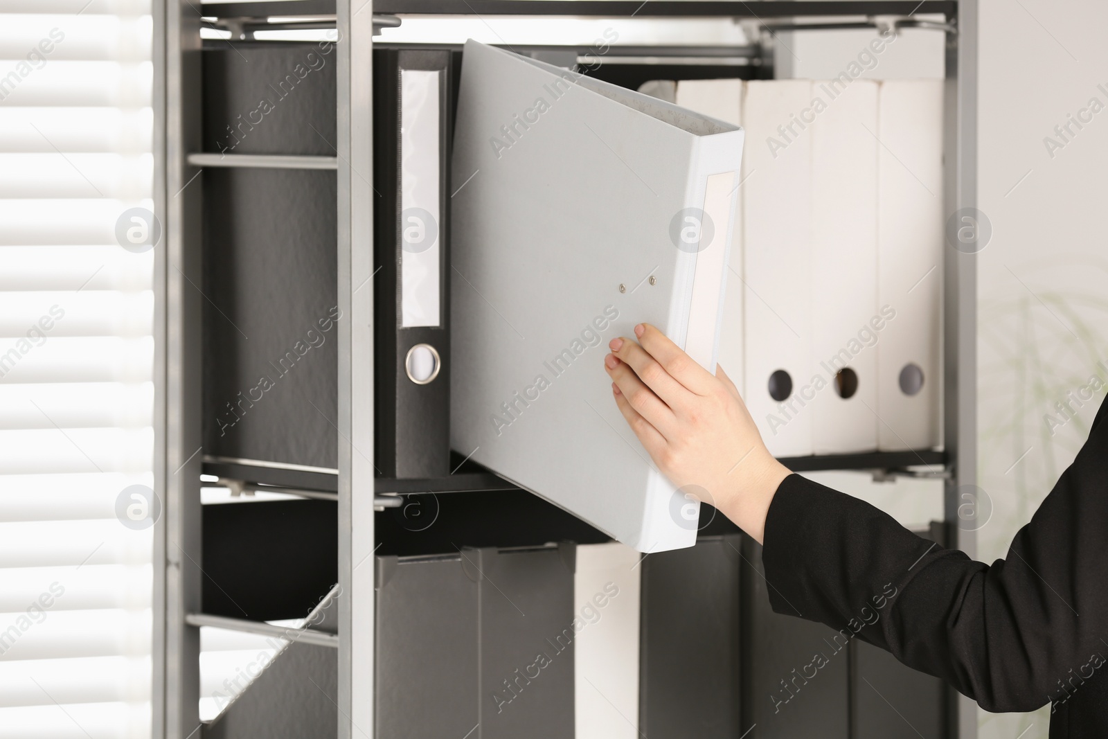 Photo of Woman taking folder with documents from shelf in office, closeup