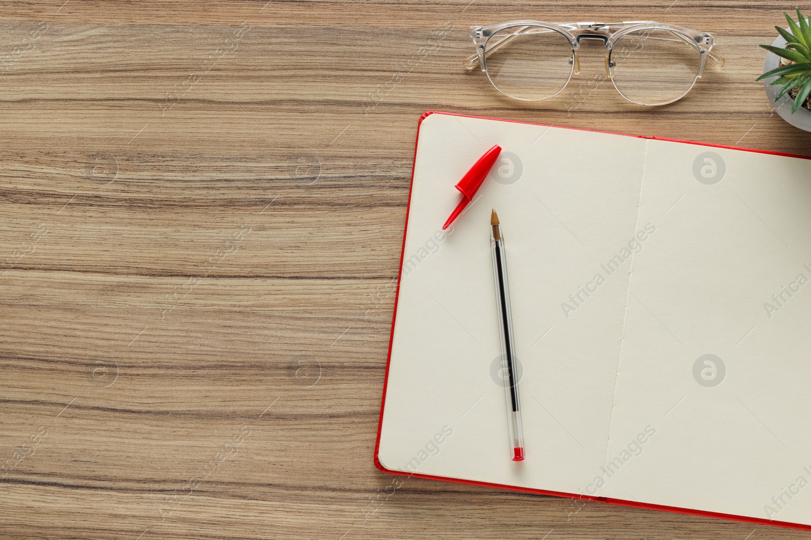 Photo of Ballpoint pen, notebook and glasses on wooden table, flat lay. Space for text