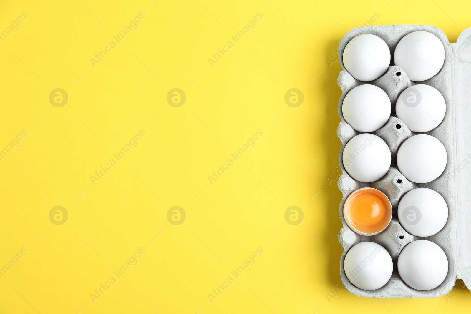 Photo of Fresh chicken eggs in box on yellow background, top view. Space for text