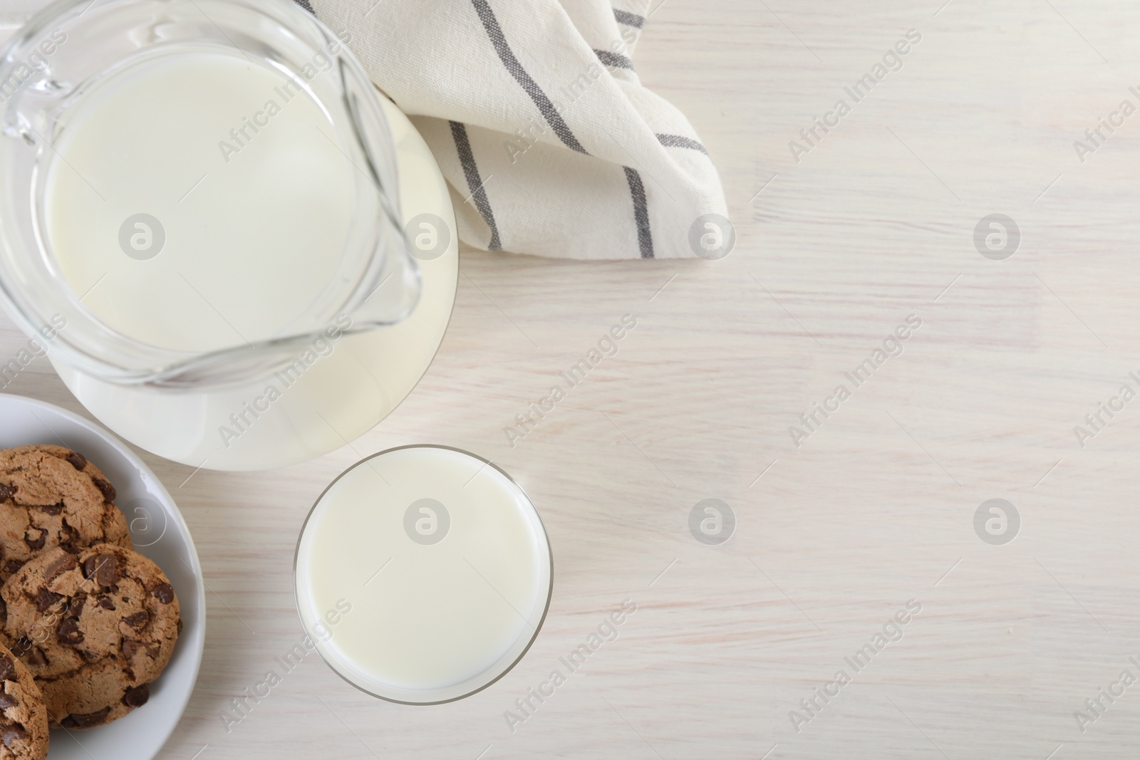 Photo of Jug of fresh milk, glass and cookies on wooden table, top view. Space for text