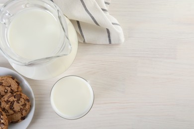 Photo of Jug of fresh milk, glass and cookies on wooden table, top view. Space for text