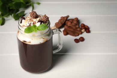 Mason jar of delicious hot chocolate with whipped cream and mint on white wooden table. Space for text