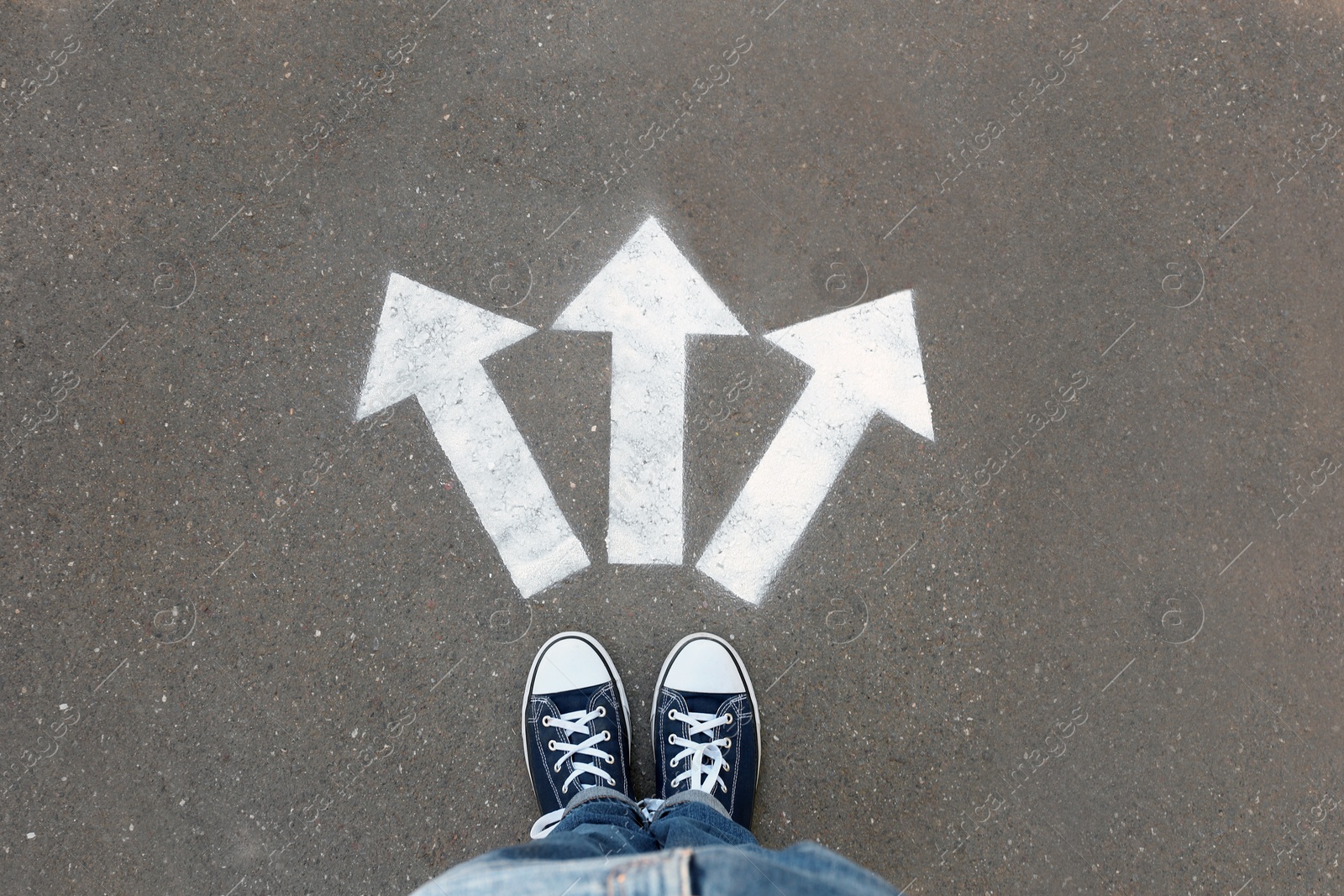 Photo of Woman standing near arrows on asphalt, top view. Choice concept