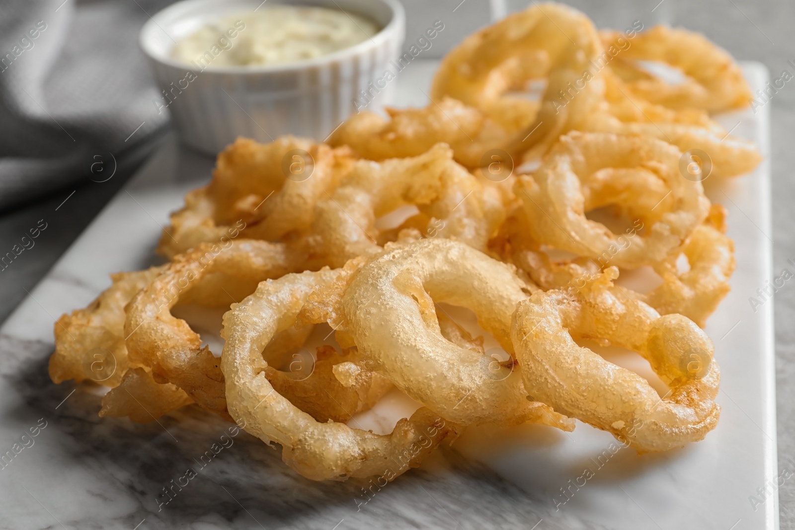 Photo of Closeup view of delicious golden breaded and deep fried crispy onion rings on marble board