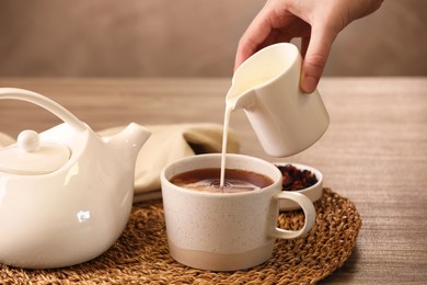 Woman pouring milk into cup with aromatic tea at wooden table, closeup