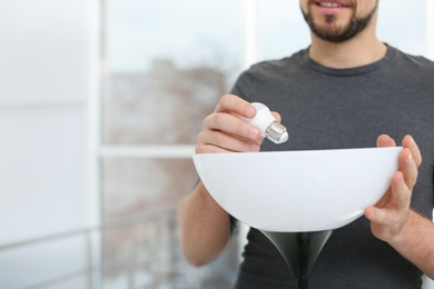 Photo of Man changing light bulb in lamp indoors, closeup with space for text