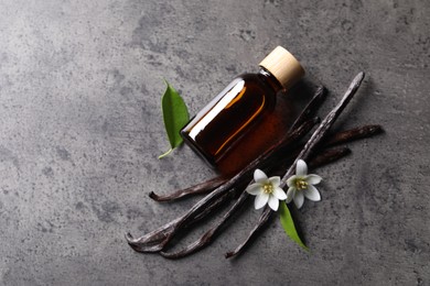 Photo of Vanilla pods, flowers, leaves and bottle with essential oil on grey textured table, flat lay. Space for text