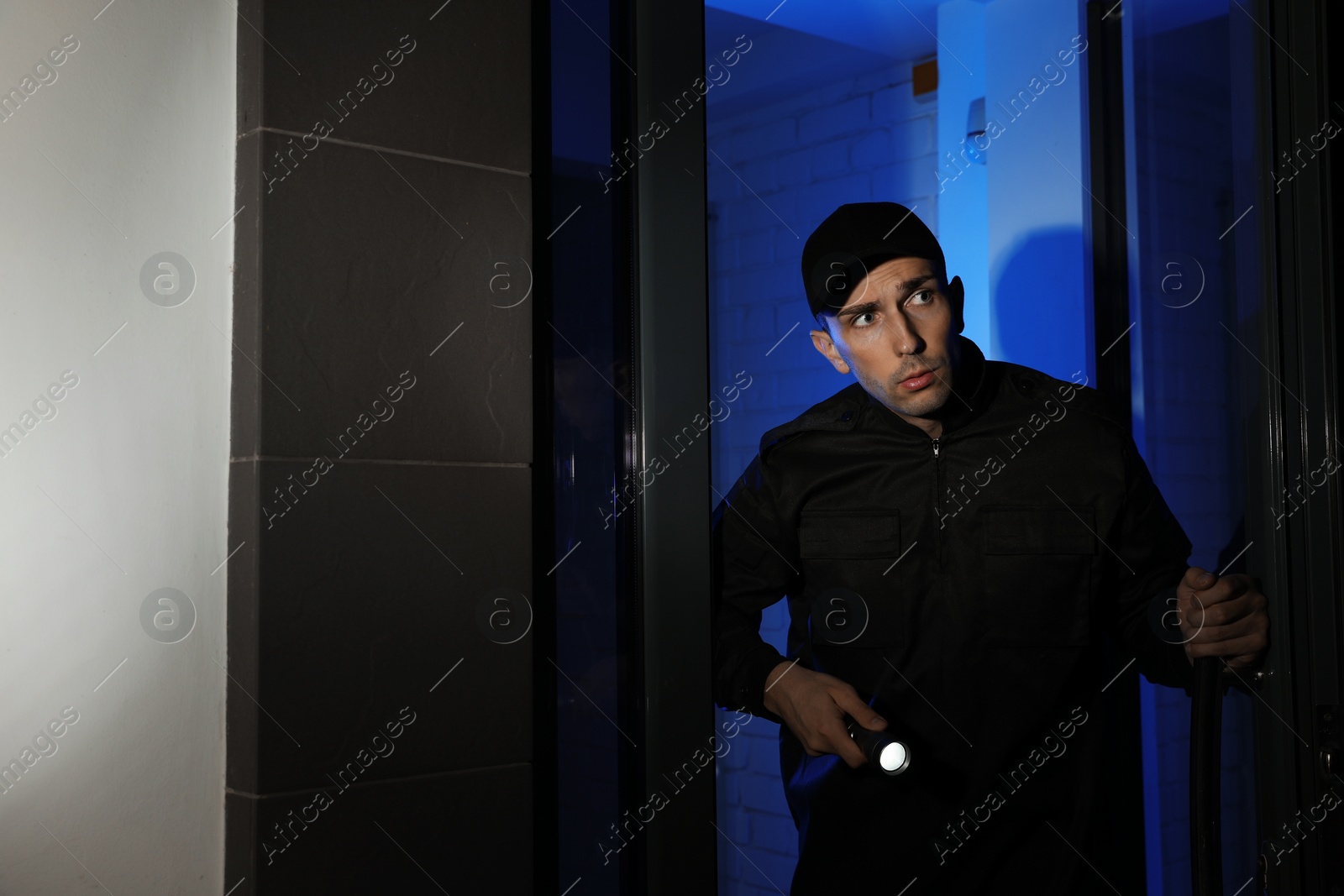 Photo of Male security guard with flashlight near entrance door at night