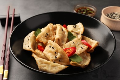 Photo of Delicious gyoza (asian dumplings) in bowl and chopsticks on gray table, closeup