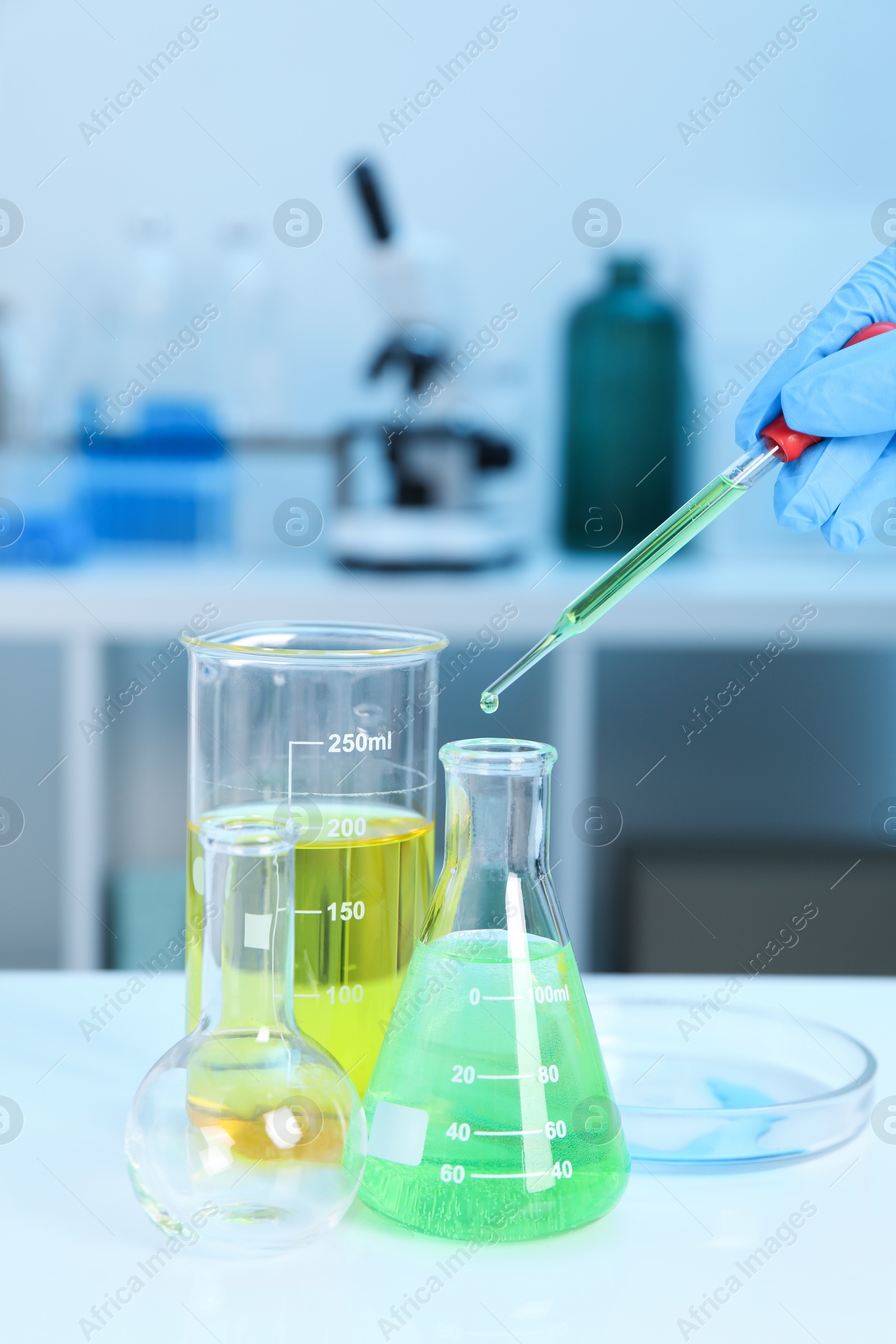 Photo of Laboratory analysis. Woman dripping liquid into flask at white table indoors, closeup