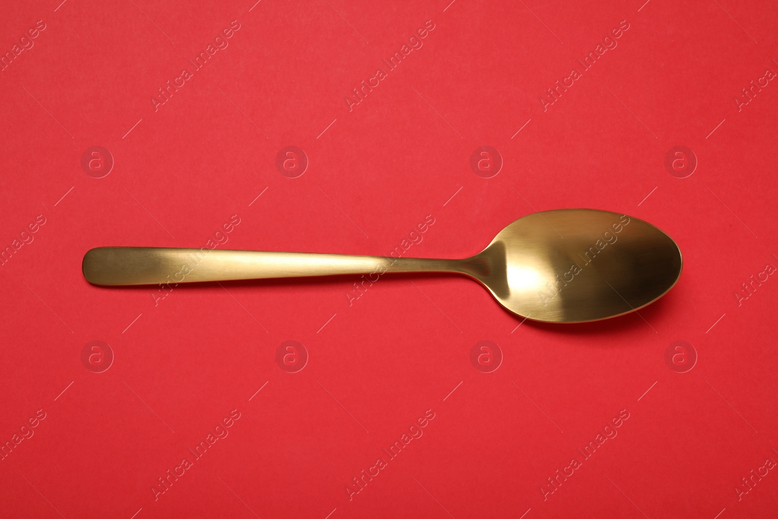 Photo of One shiny golden spoon on red background, top view