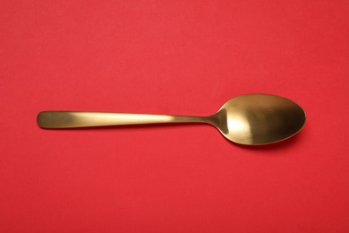 One shiny golden spoon on red background, top view