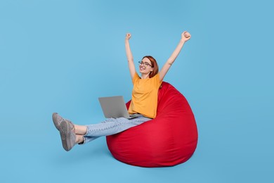 Photo of Happy young woman with laptop sitting on beanbag chair against light blue background, space for text