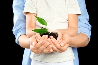 Woman and her child holding soil with green plant in hands on black background. Family concept