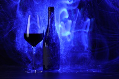 Photo of Red wine in glass and bottle in blue lights, space for text