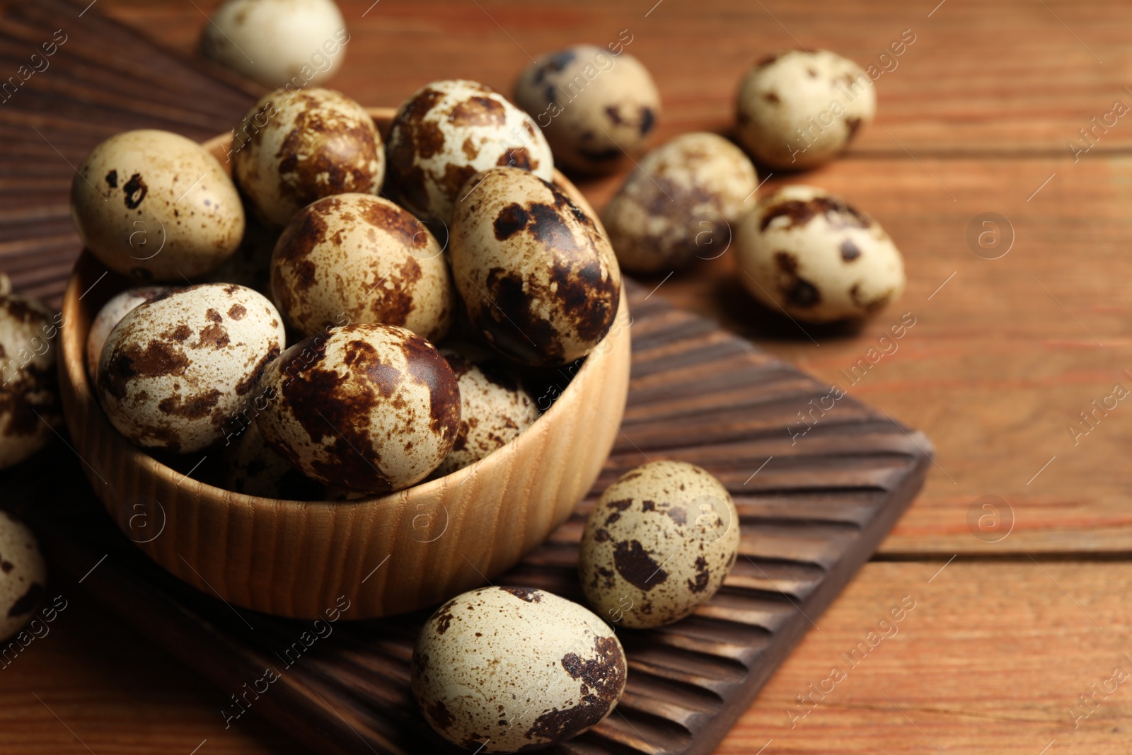 Photo of Bowl and many speckled quail eggs on wooden table, space for text