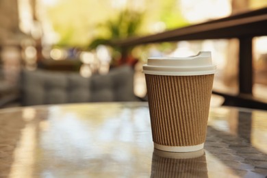 Takeaway paper coffee cup on table in outdoor cafe. Space for text