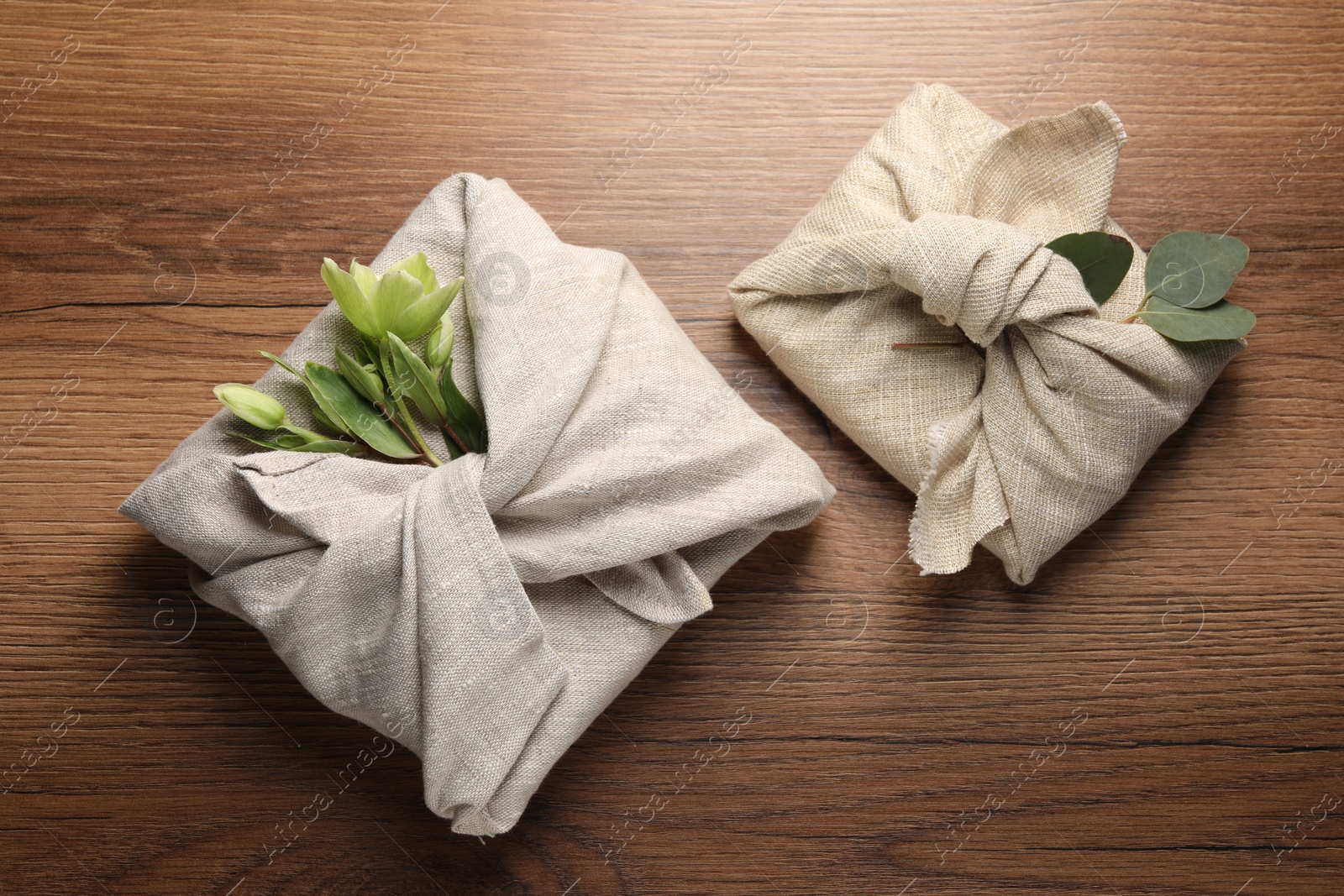 Photo of Furoshiki technique. Gift packed in different fabrics decorated with plants on wooden table, flat lay