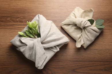 Furoshiki technique. Gift packed in different fabrics decorated with plants on wooden table, flat lay