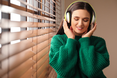 Young woman listening to audiobook near window indoors