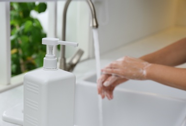 Photo of Bottle of antibacterial soap and woman washing hands on background. Personal hygiene during COVID-19 pandemic