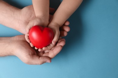 Father and his child holding red decorative heart on light blue background, top view. Space for text