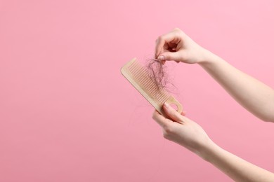 Photo of Woman untangling her lost hair from comb on pink background, closeup and space for text. Alopecia problem