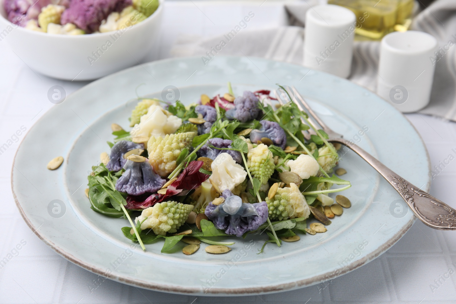 Photo of Delicious salad with cauliflower and pumpkin seeds served on white tiled table, closeup