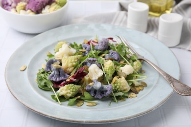 Delicious salad with cauliflower and pumpkin seeds served on white tiled table, closeup