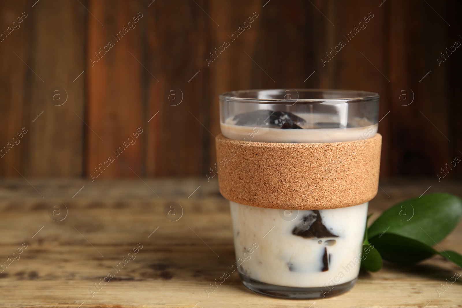 Photo of Glass of milk with grass jelly and green leaves on wooden table, closeup. Space for text