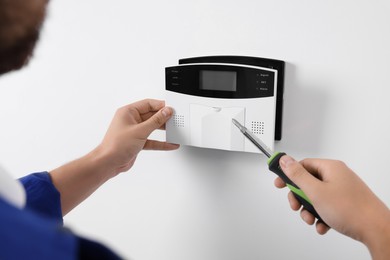 Photo of Man installing home security alarm system on white wall indoors, closeup
