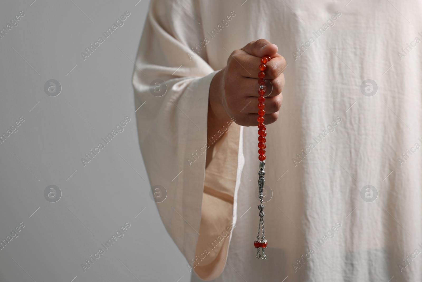 Photo of Muslim man with misbaha on light grey background, closeup. Space for text