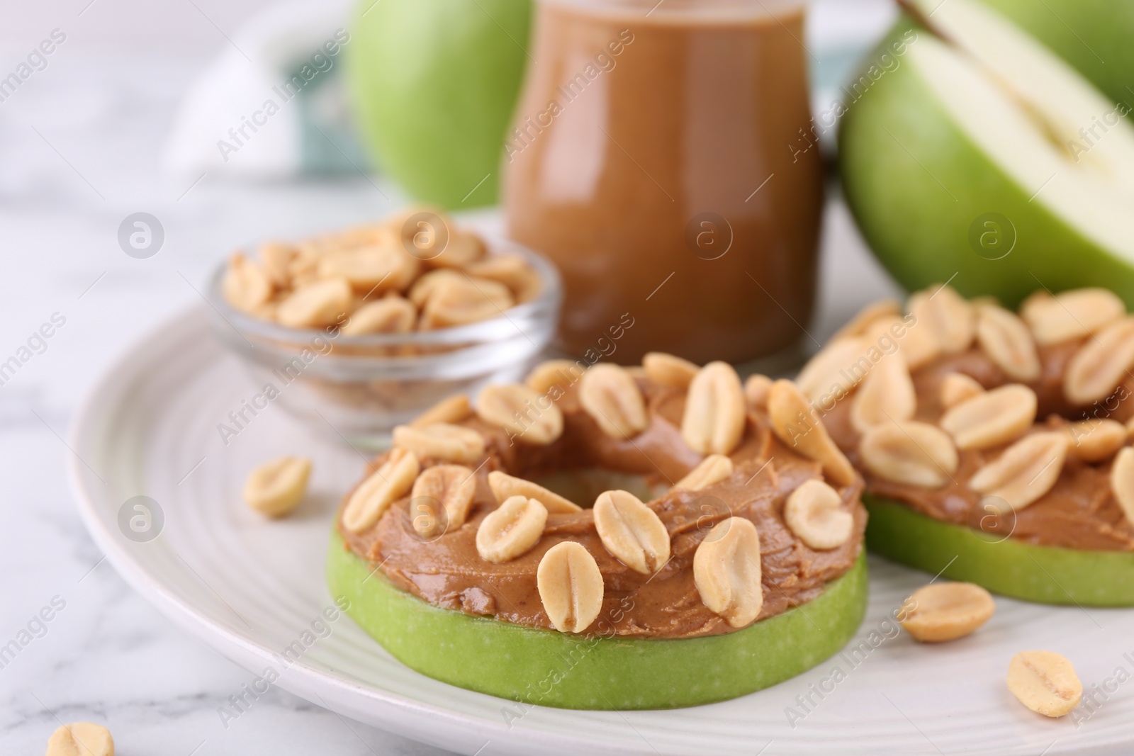 Photo of Slices of fresh apple with peanut butter and nuts on white marble table, closeup