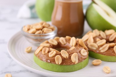 Slices of fresh apple with peanut butter and nuts on white marble table, closeup