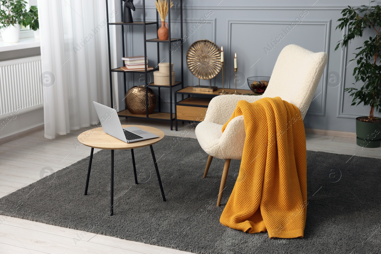 Photo of Living room interior with comfortable armchair, blanket and side table