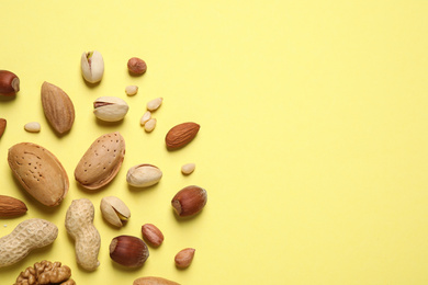 Different delicious nuts on yellow background, flat lay. Space for text