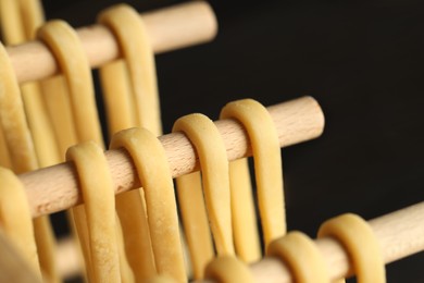 Photo of Homemade pasta drying on wooden rack against dark background, closeup