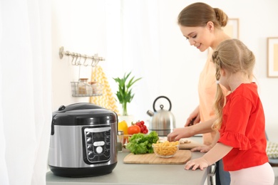 Mother and daughter preparing food near modern multi cooker in kitchen