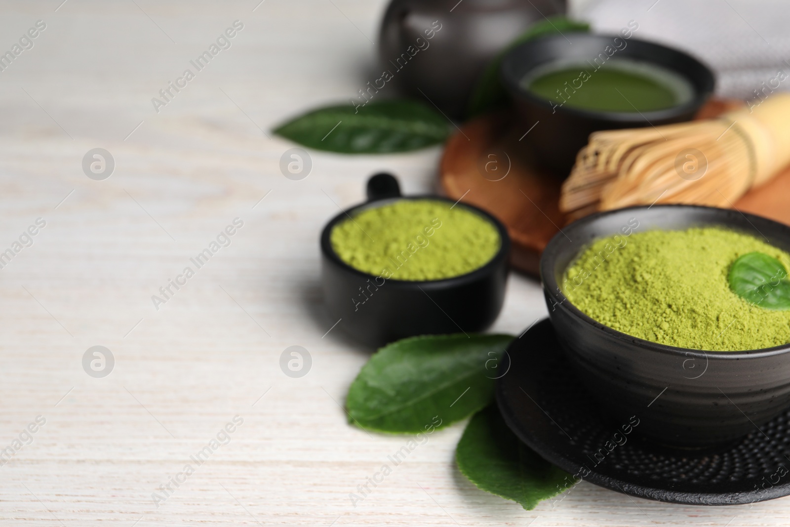 Photo of Green matcha powder and leaves on white wooden table, closeup. Space for text