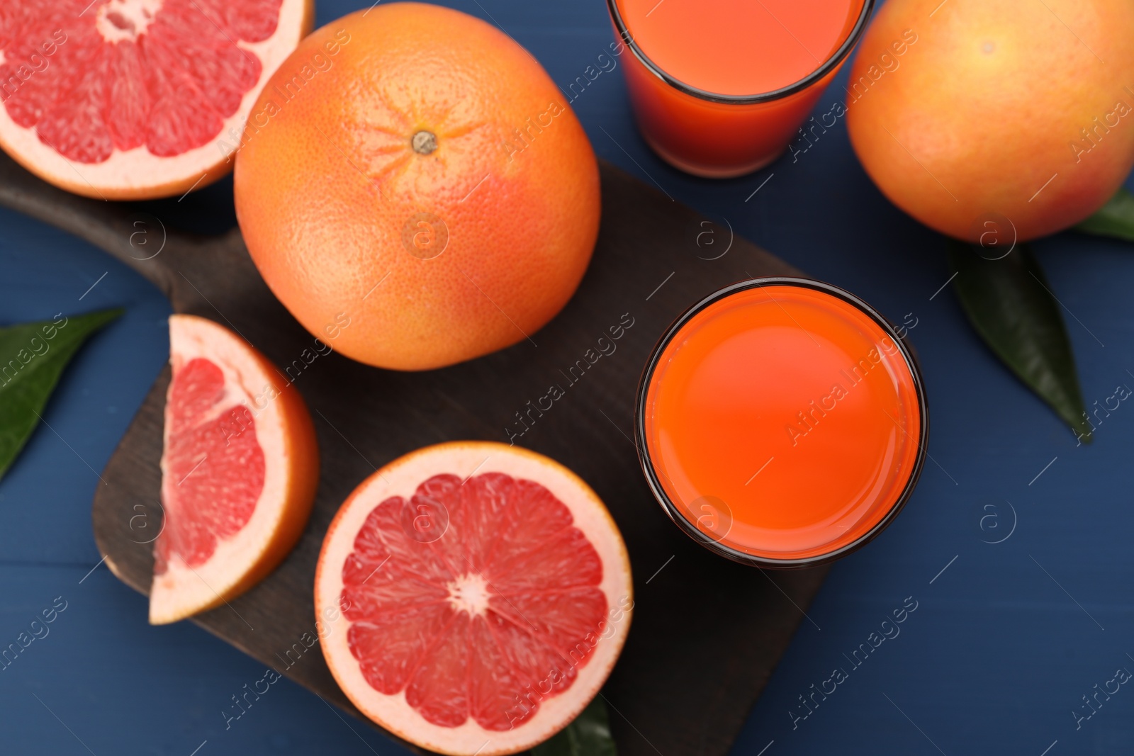 Photo of Tasty grapefruit juice in glasses and fresh fruits on blue wooden table, flat lay