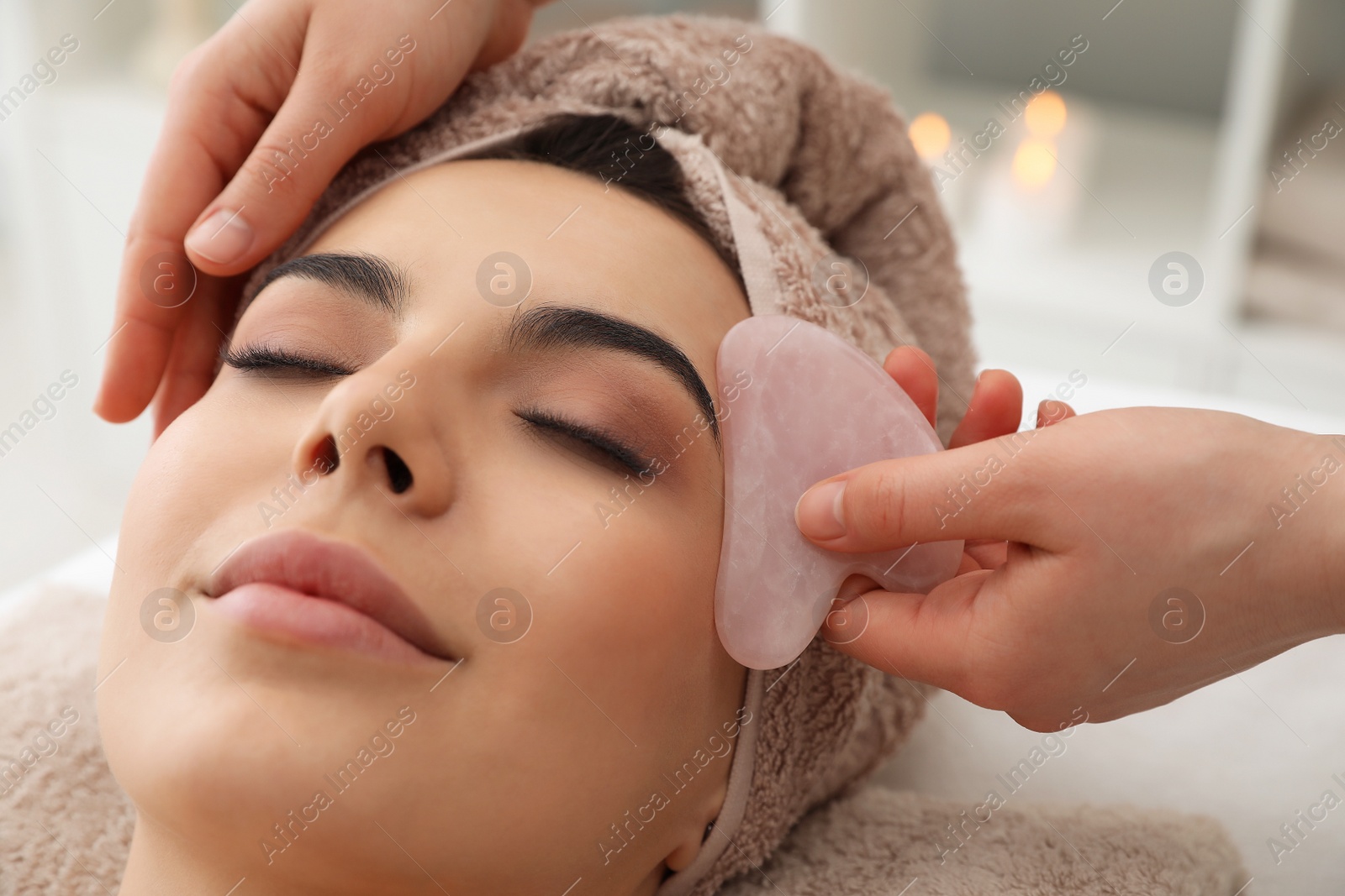 Photo of Young woman receiving facial massage with gua sha tool in beauty salon, closeup