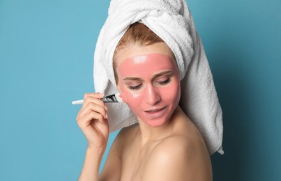 Young woman applying pomegranate face mask on light blue background