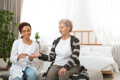 Doctor measuring patient's blood sugar level with digital glucose meter at home. Diabetes control