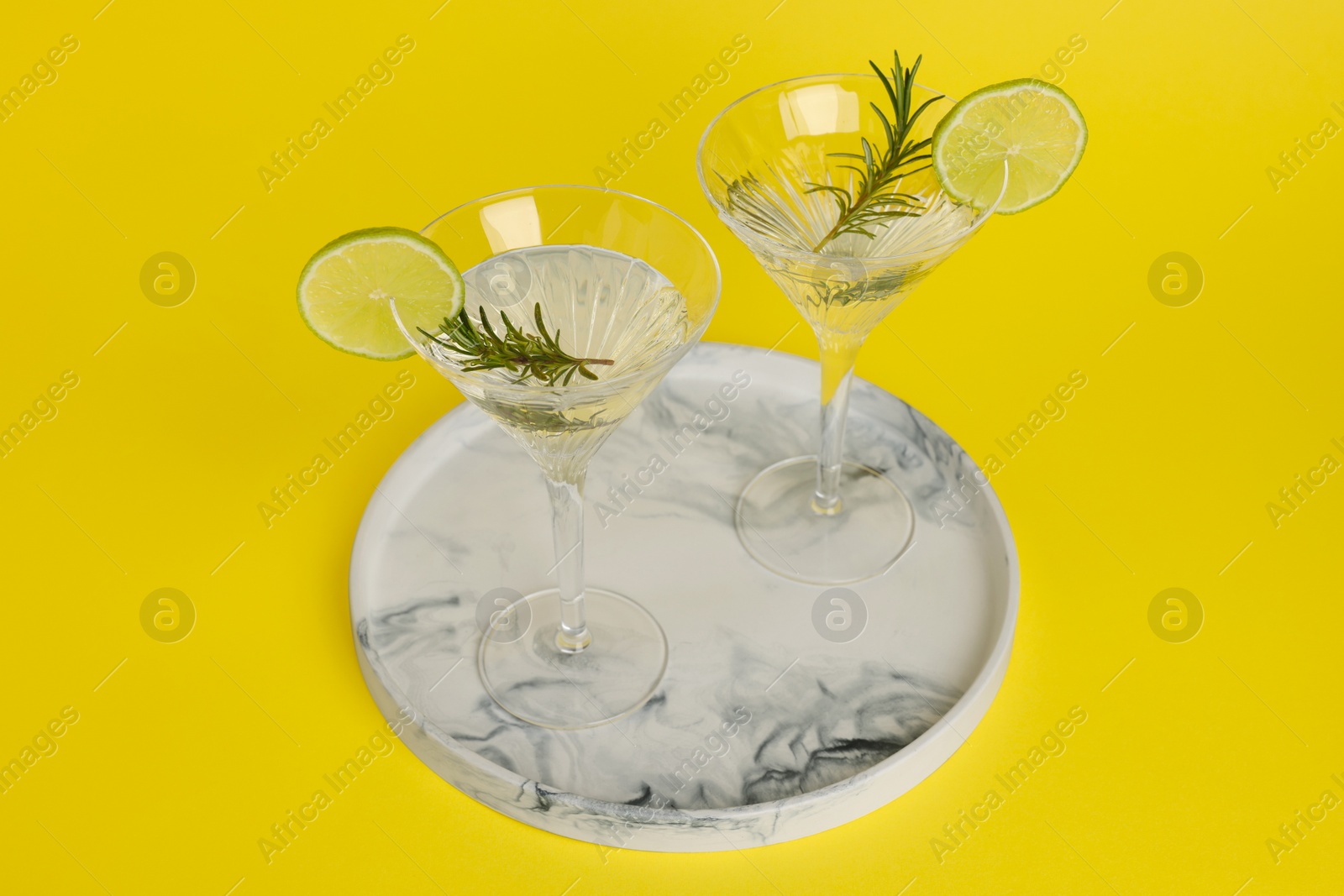 Photo of Martini glasses of refreshing cocktail with lemon slices and rosemary on yellow background