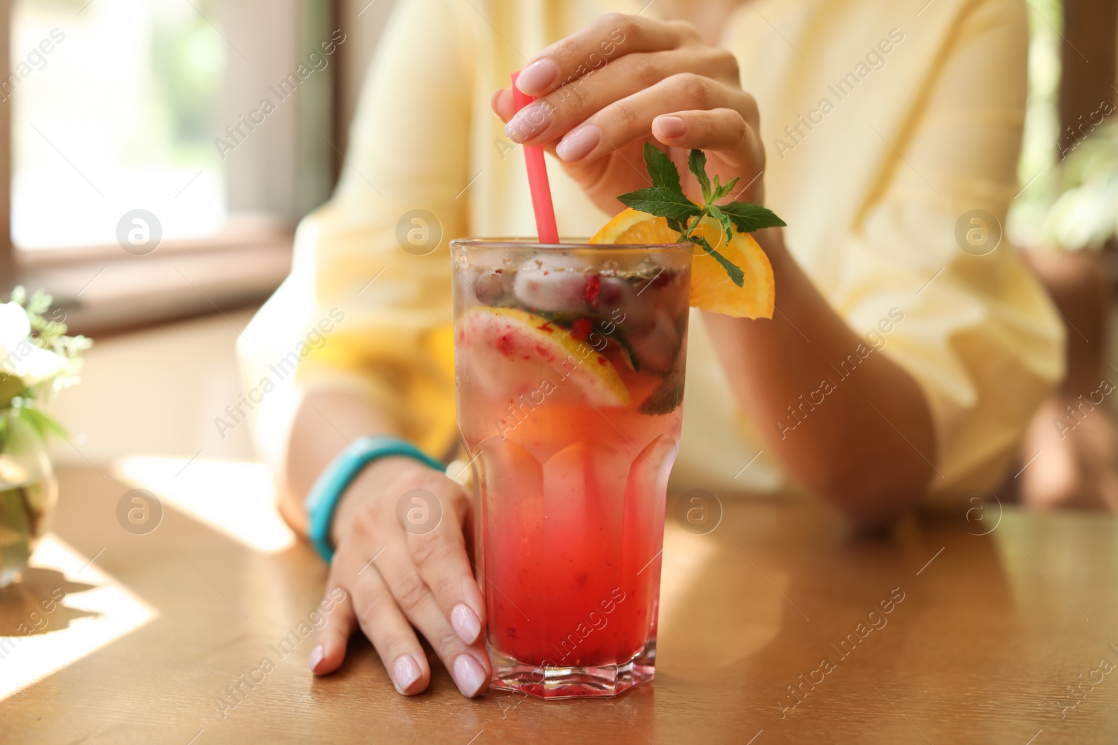 Photo of Young woman with glass of tasty natural lemonade in cafe, closeup. Detox drink