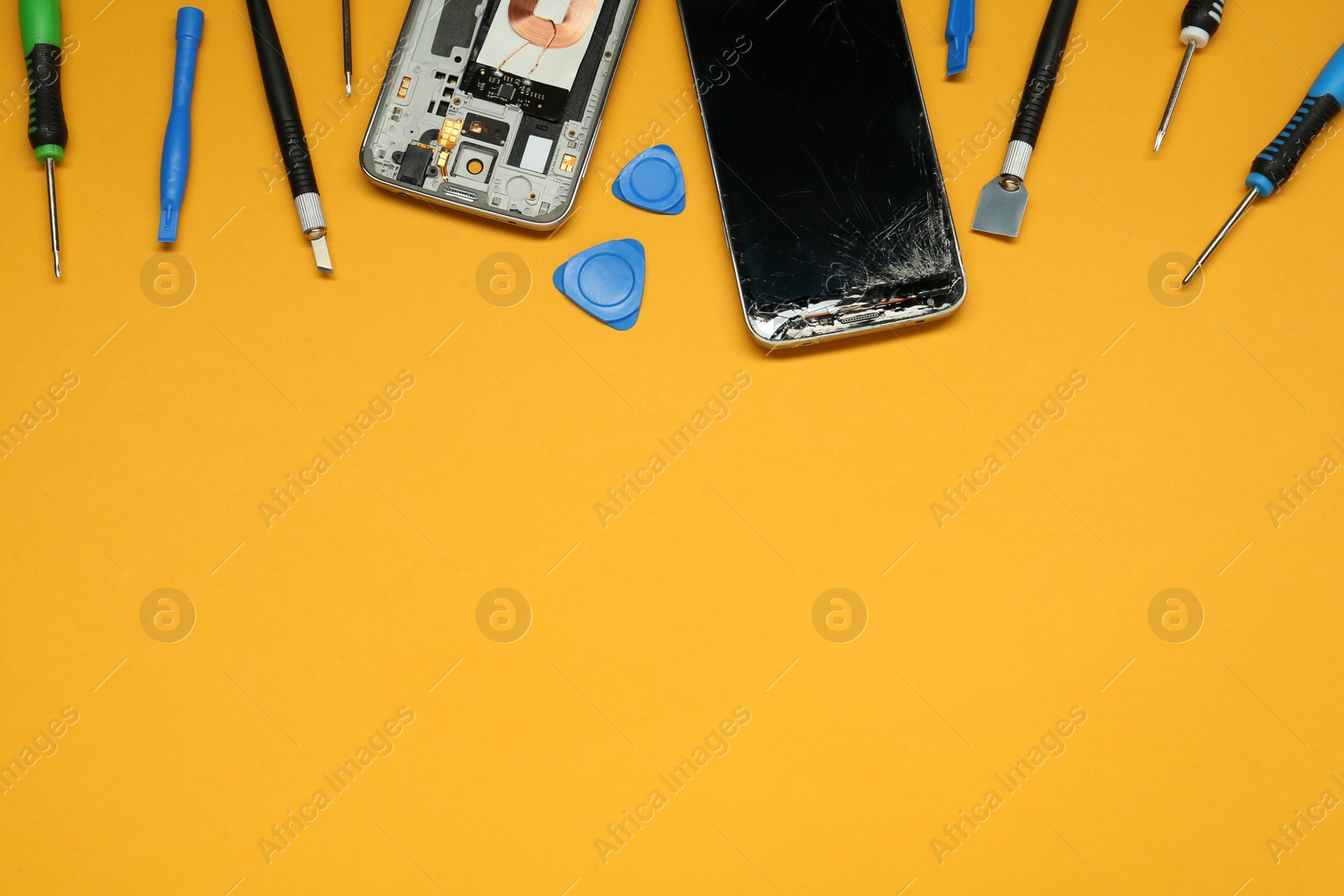 Photo of Damaged smartphone and repair tool set on orange background, flat lay. Space for text